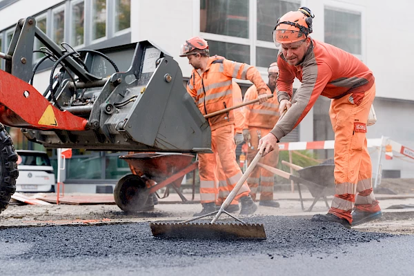 Construction worker spreading asphalt on a Bern street – precise craftsmanship captured through sustainable construction photography.