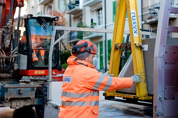 Construction worker handling a lifting device beside a site vehicle in Bern – safe material handling and precise site coordination.