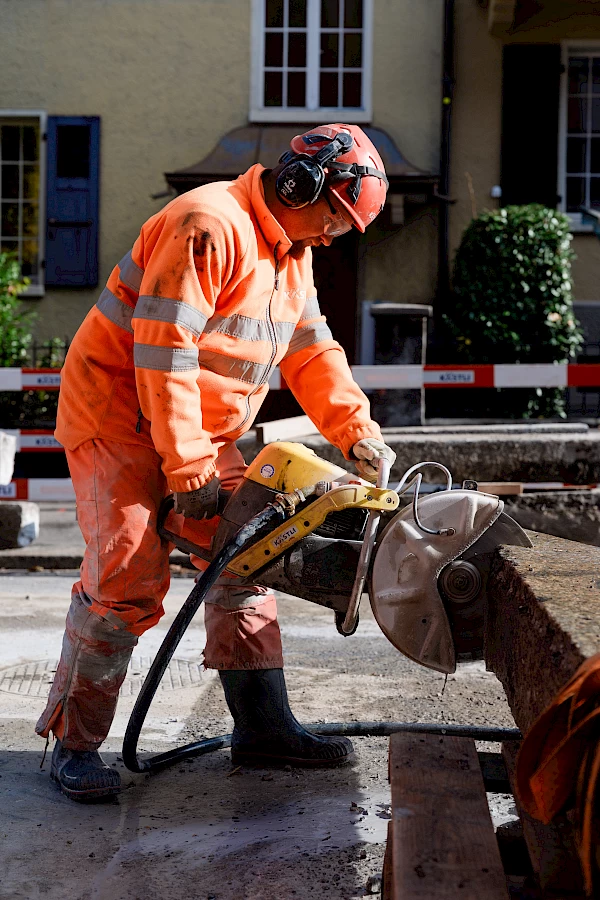 Construction worker cutting concrete with a power saw on a Bern site – capturing precision craftsmanship and safety in action.